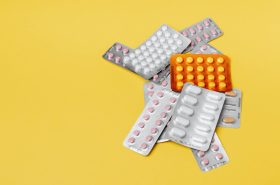 Keltaisella taustalla on värikas kasa erilaisia pilleriläpipainopakkauksia